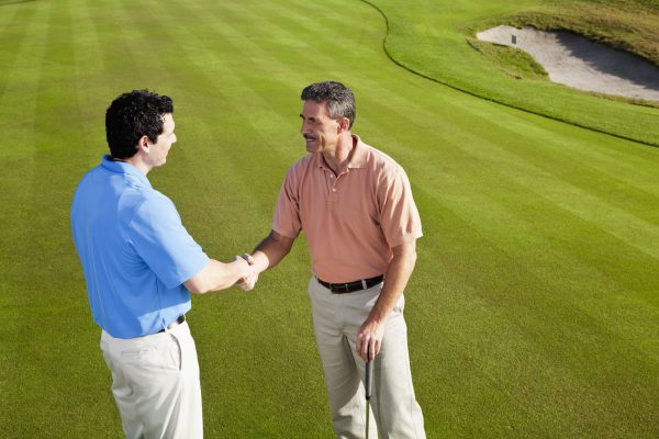 Men on golf course putting green shaking hands