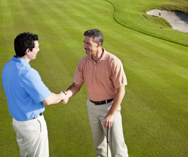 Men on golf course putting green shaking hands