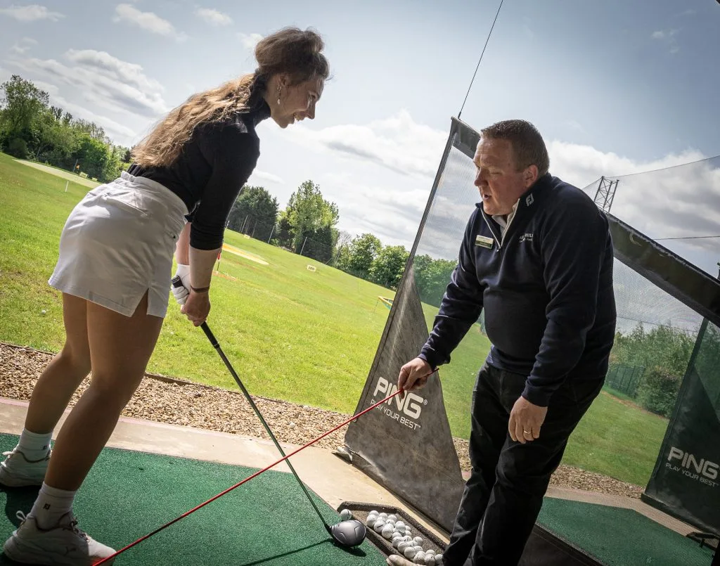 Golf lessons with man teaching female golfer using alignment sticks in Milton Keynes