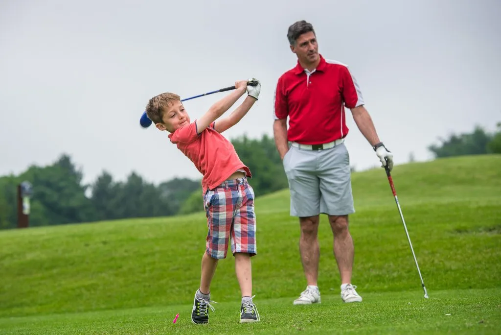 child hitting the ball behind adult at golf course in milton keynes
