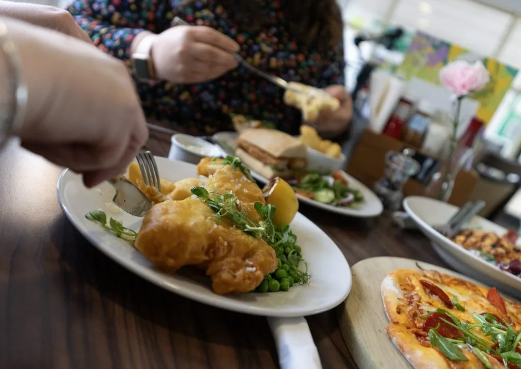 family enjoying food, cutting fish and chips at a restaurant near milton keynes