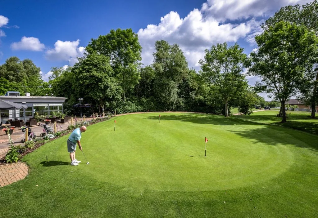 Man putting on a practice putting green at a golf club in Milton Keynes