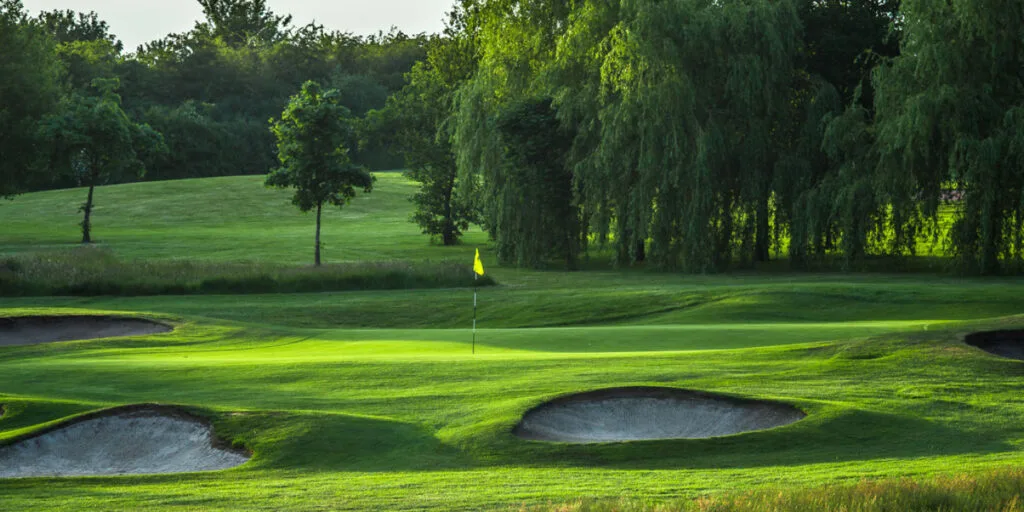 Beautiful golf hole with sun rays shining across the green, showcasing one of the top golf courses milton keynes