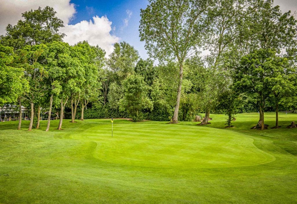 A neat golf green surrounded by trees on an 18 hole golf course in Milton Keynes